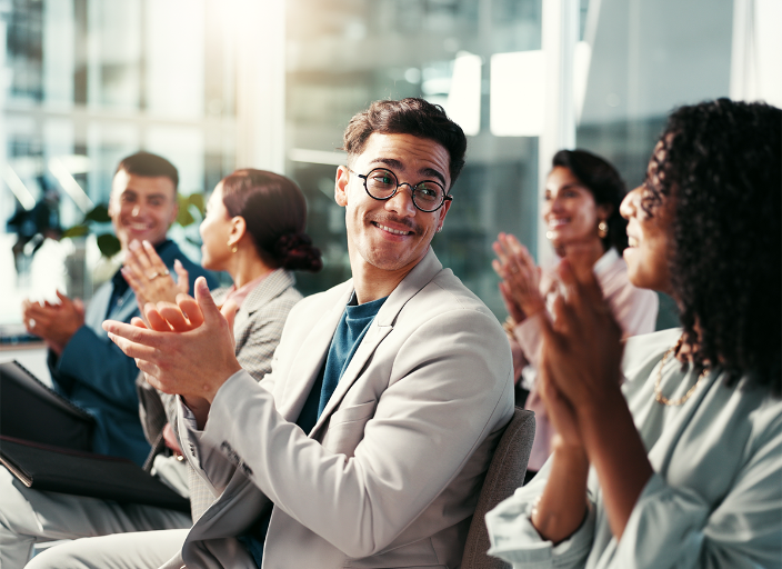Grupo de personas sentadas aplaudiendo y sonriendo en una sala.