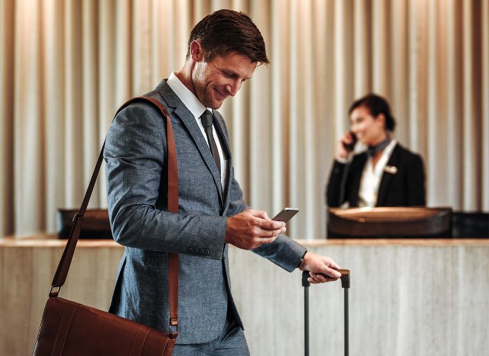 Ejecutivo con maleta revisa su celular en la recepción de un hotel.