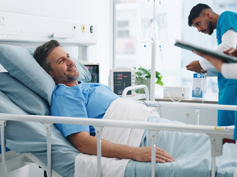 Paciente adulto ingresado en una habitación de hospital mientras un profesional de la salud revisa su historial