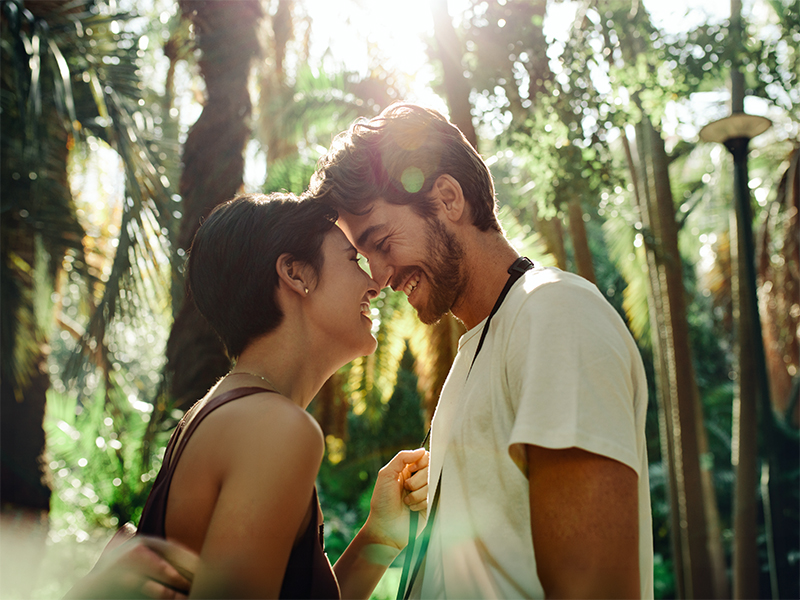 Pareja sonríe frente con frente bajo las palmeras.