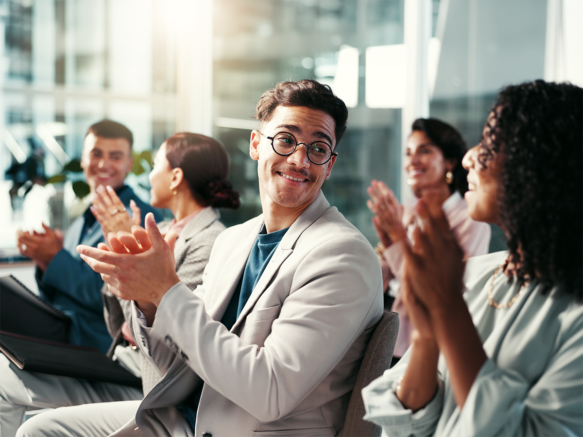 Grupo de personas sentadas aplaudiendo y sonriendo en una sala.