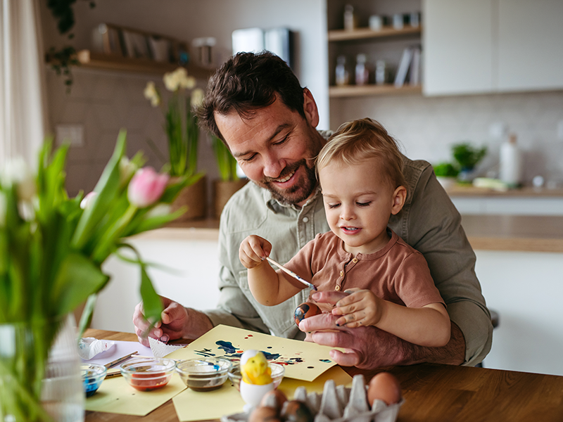 Padre pinta con su hijo pequeño en la mesa de la cocina.