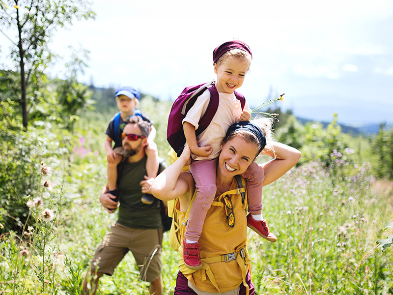 Padres caminan por el campo con sus dos hijos a hombros.